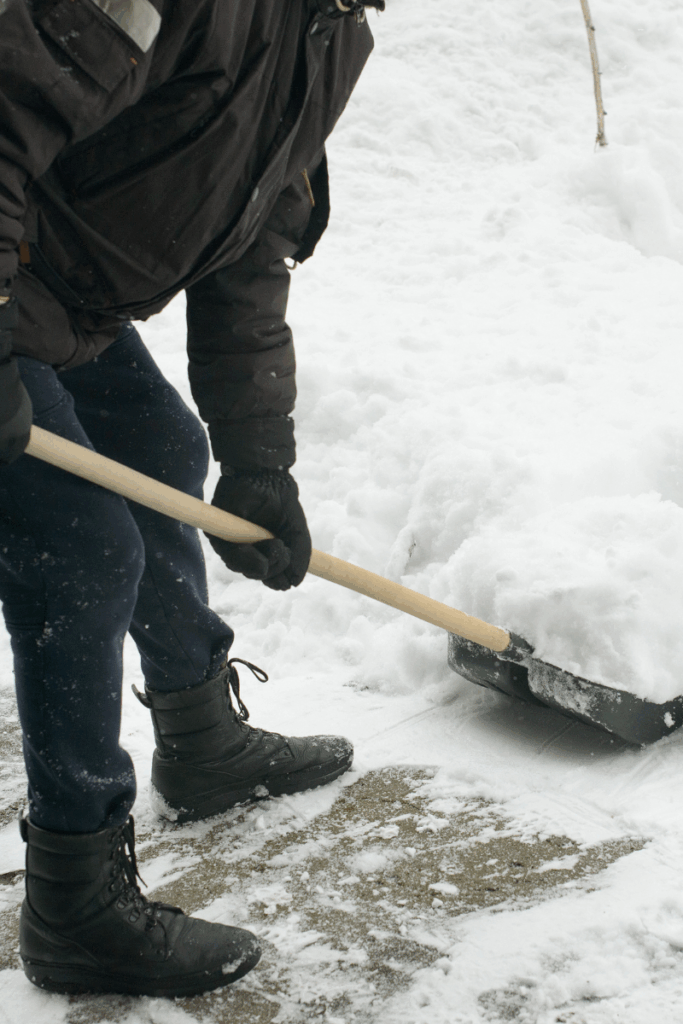Person shoveling heavy snow and experiencing winter back pain.
