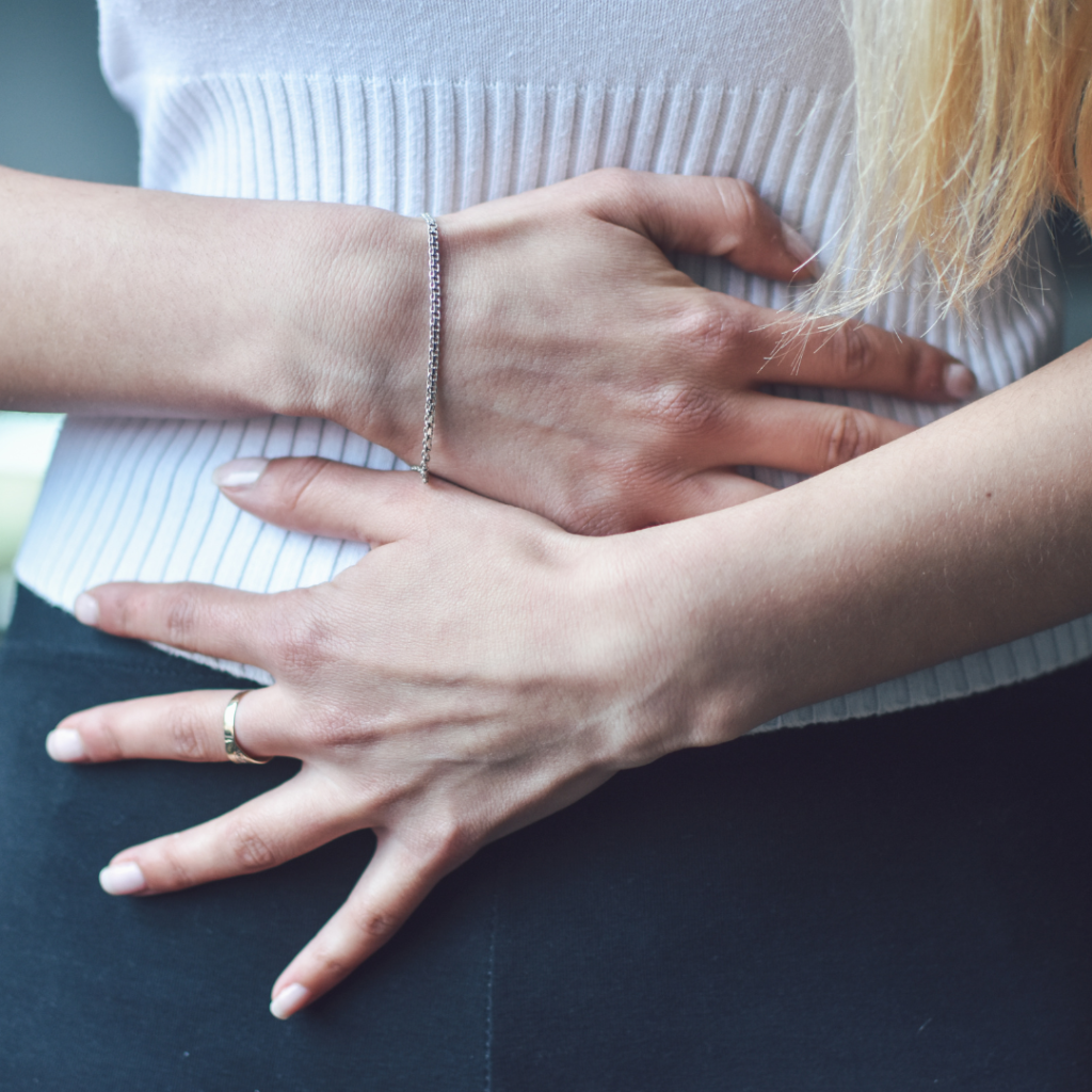Woman covering her lower abdomen to show pelvic floor symptoms like leaking.